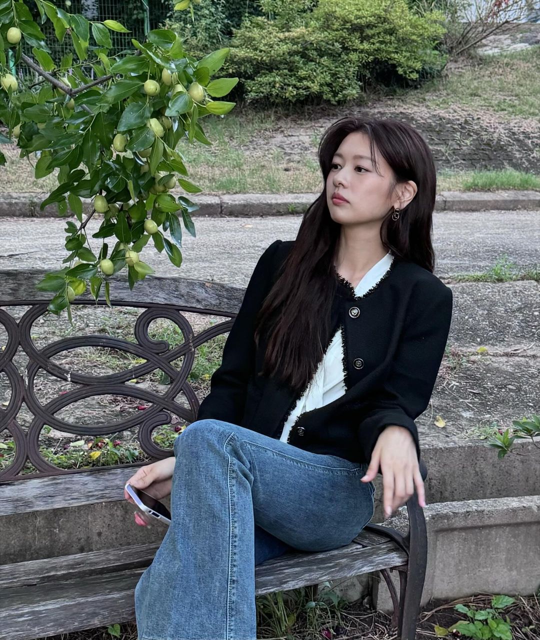 calo - diễn viên Jung So Min mặc áo cardigan màu đen phối với quần jeans, tạo dáng ngồi trên ghế để chụp ảnh ngoài trời